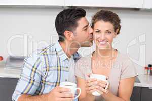 Cheerful woman drinking coffee getting a kiss from partner