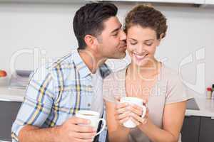 Happy woman drinking coffee getting a kiss from partner