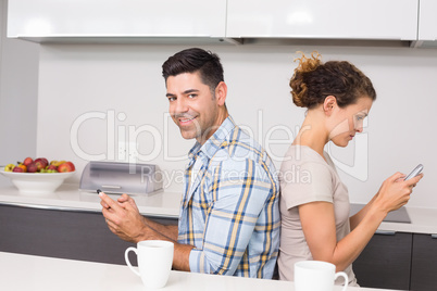 Couple sitting back to back texting with man smiling at camera