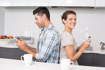 Smiling couple sitting back to back texting