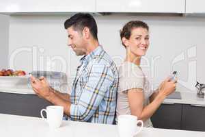 Smiling couple sitting back to back texting
