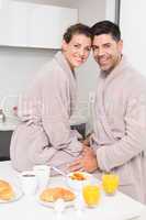 Smiling couple in bathrobes having breakfast together