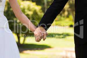 Mid section of newlywed couple holding hands in park