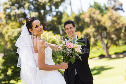 Happy newlywed couple with bouquet in park