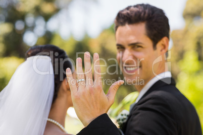 Bridegroom showing wedding ring to the camera in park