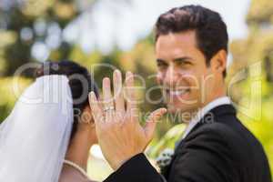 Bridegroom showing wedding ring to the camera in park