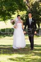 Newlywed couple holding hands and walking in park