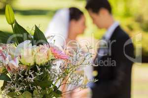 Bouquet with blurred newlywed couple in background at park