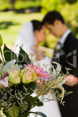 Bouquet with blurred newlywed couple in background at park