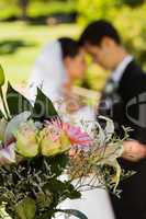 Bouquet with blurred newlywed couple in background at park