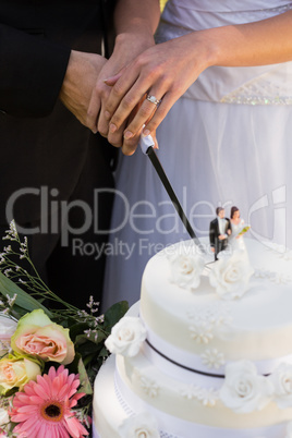 Mid section of newlywed cutting wedding cake