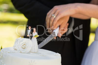 Mid section of a newlywed cutting wedding cake