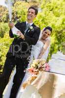 Newlywed couple with groom opening champagne bottle at park