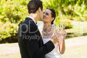 Newlywed kissing while toasting champagne flutes at park