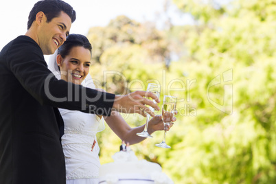 Newlywed toasting champagne flutes besides cake at park