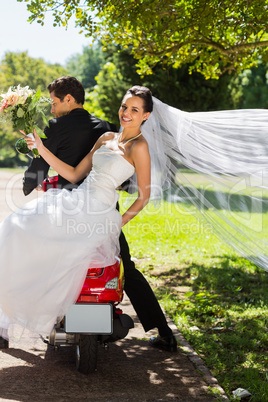 Newlywed couple sitting on scooter in park