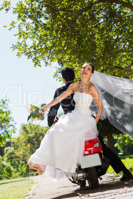 Newlywed couple sitting on scooter in park