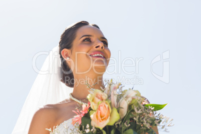 Smiling beautiful bride with bouquet against clear sky