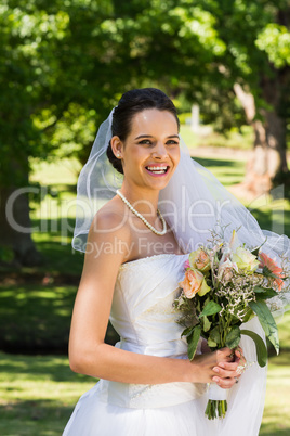 Smiling beautiful bride with bouquet standing in park