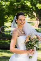 Smiling beautiful bride with bouquet standing in park