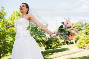 Cheerful young beautiful bride with bouquet in park