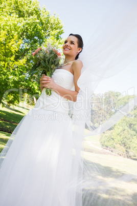 Happy young beautiful bride with bouquet in park