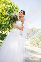 Happy young beautiful bride with bouquet in park