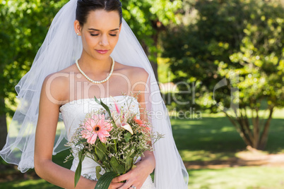 Serious beautiful bride with bouquet in park