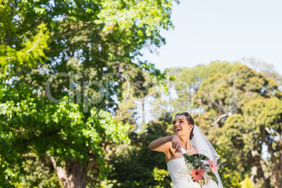 Cheerful bride throwing bouquet in park