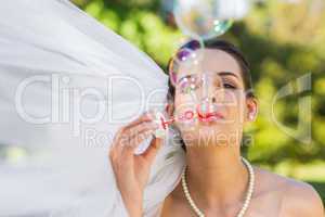 Bride blowing soap bubbles in park