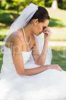 Beautiful worried bride sitting at park
