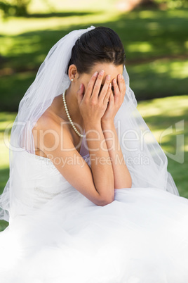 Beautiful worried bride sitting at park