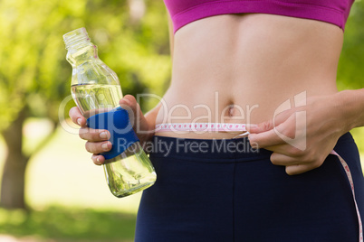Mid section of a toned woman measuring waist in park