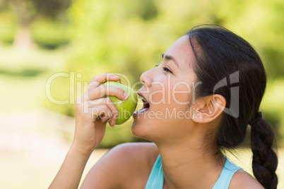 Healthy young woman eating apple in park