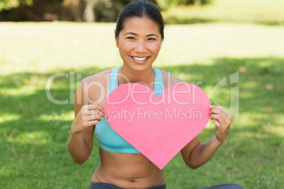 Cheerful woman holding heart shape board in park