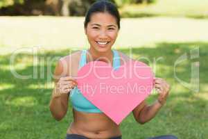 Cheerful woman holding heart shape board in park