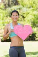 Smiling woman holding heart shape board in park