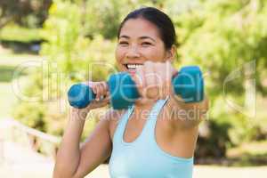 Healthy smiling woman exercising with dumbbells in park