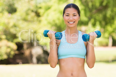 Healthy smiling woman exercising with dumbbells in park