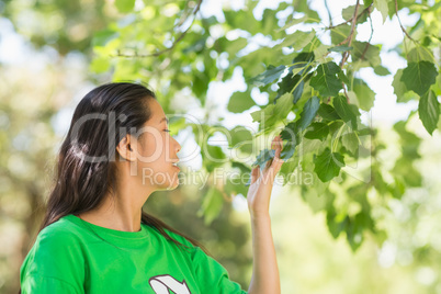 Woman in green recycling t-shirt smelling leaves at park