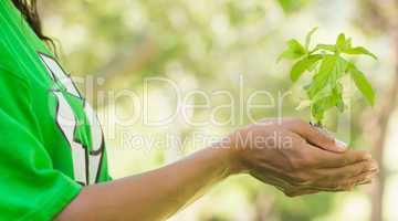 Mid section of woman in recycling t-shirt holding young plant