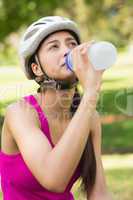 Fit young woman in helmet drinking water at park