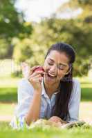 Woman eating apple while reading a book in park