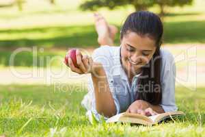 Woman eating apple while reading a book in park