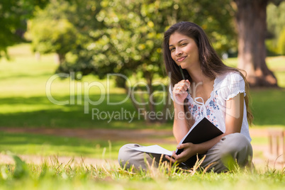 Young woman with book and pen sitting in park