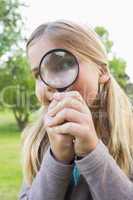 Cute young girl looking through magnifying glass at park