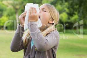 Girl sneezing into tissue paper at park