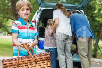 Boy with picnic basket while family in background at car trunk