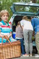 Boy with picnic basket while family in background at car trunk