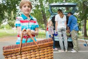 Boy with picnic basket while family in background at car trunk